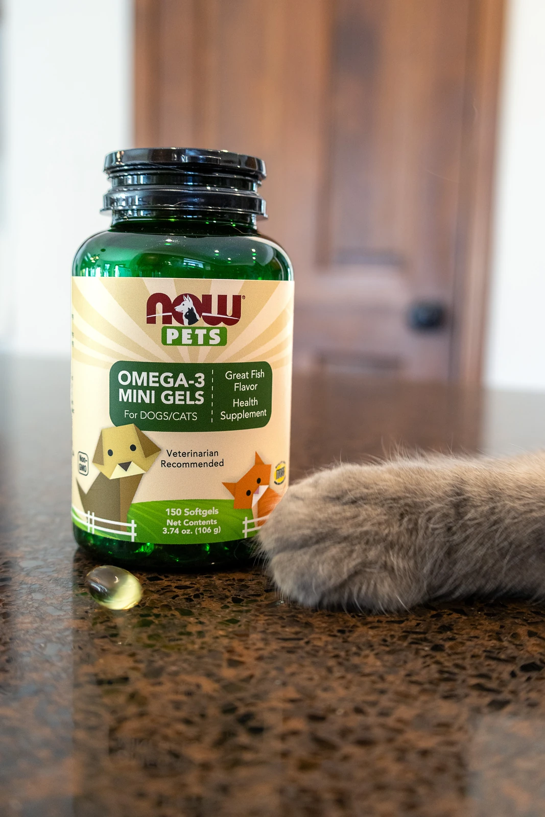 A calico cat resting beside a bottle of NOW Pets Omega-3 Mini Gels in warm light